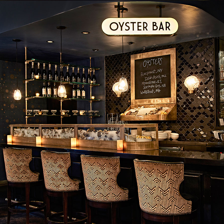 The Oyster Bar at the Roxy Hotel, which includes wall tiles in the shape of fish scales, shell shaped lights, and a sign that reads "Oyster Bar"