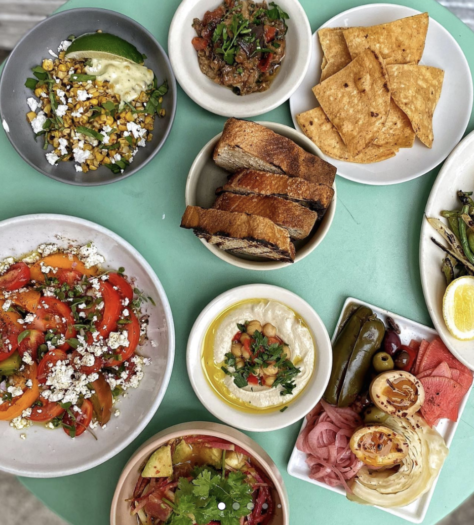 Table filled with of colorful dishes from Lighthouse, including different kinds of fresh salads, toasted bread, a plate of hummus and other dips, and an array of pickled vegetables