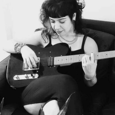 Melanie Giselle on a couch playing guitar