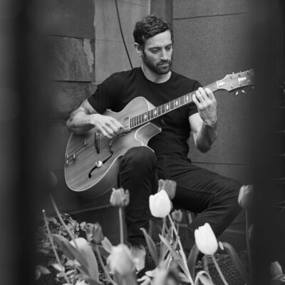 Matthew Avedon playing guitar and sitting on a stool
