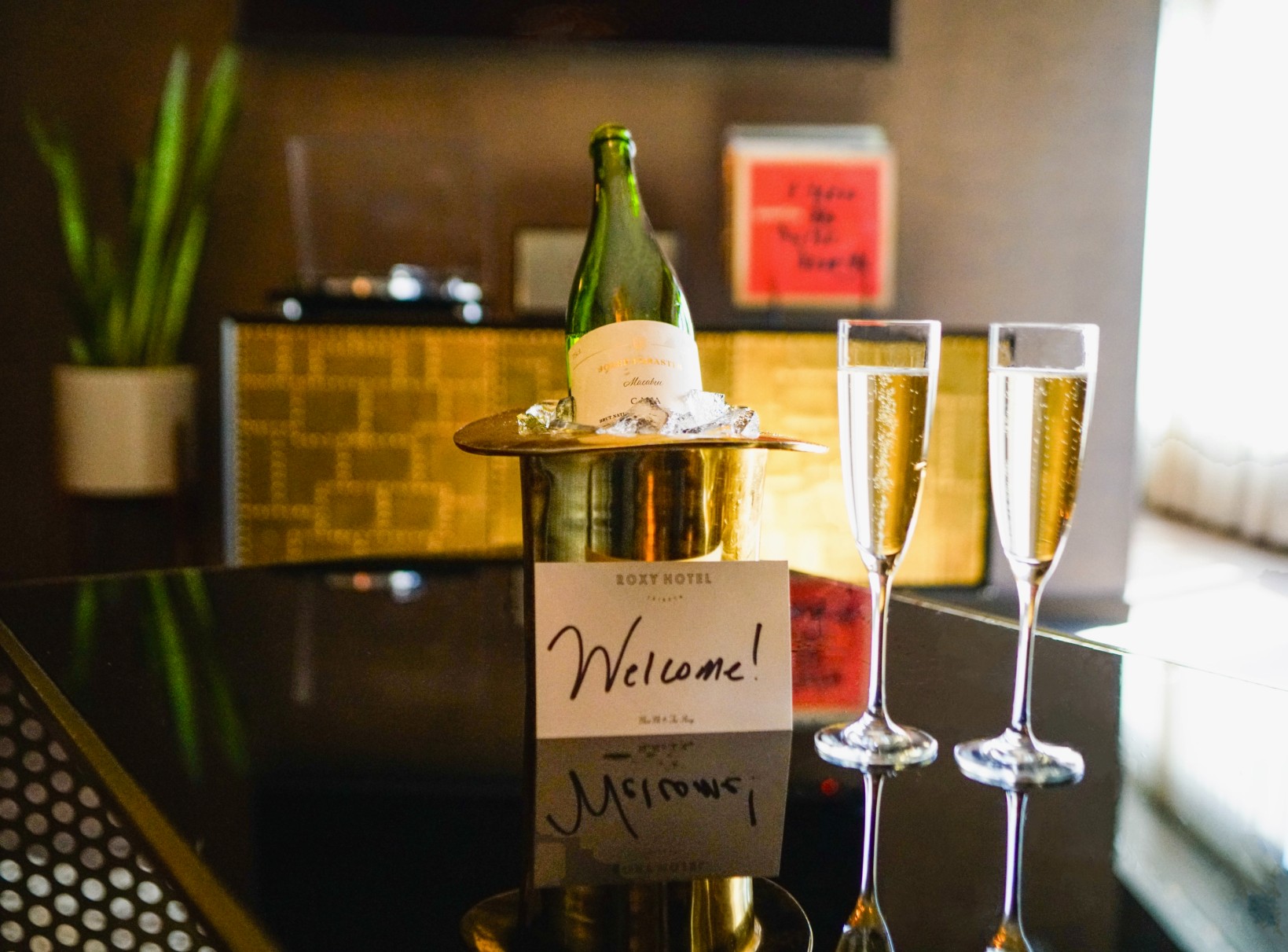 Champagne bottle on ice with two champagne glasses on black table.