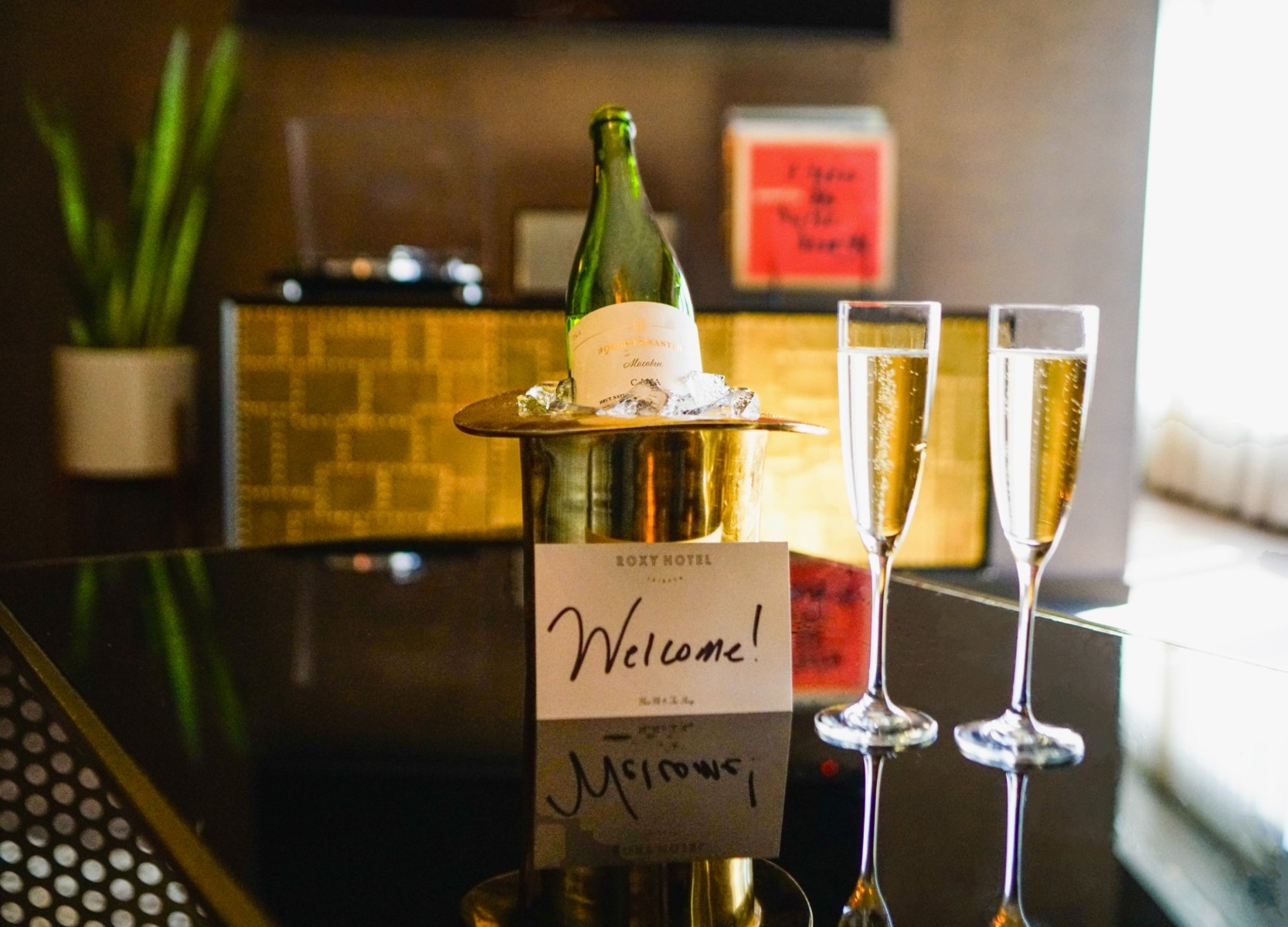Champagne bottle on ice with two champagne glasses on black table.